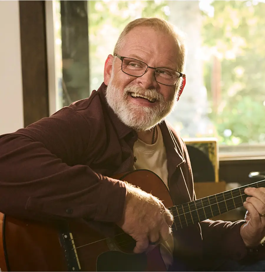 A portrait of a smiling older man playing guitar.