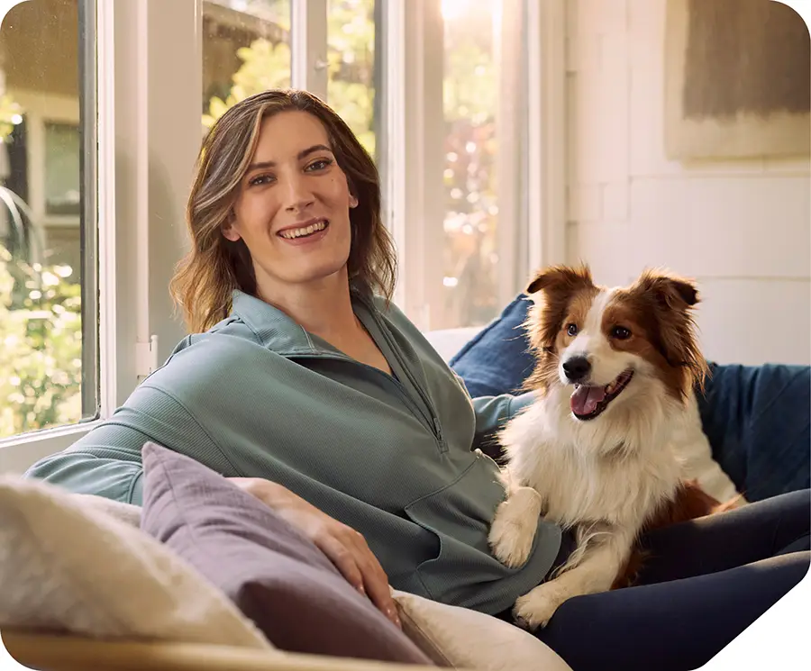 A younger woman smiling, sitting on couch with dog.