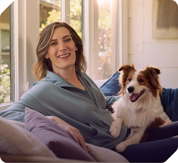 A younger woman smiling, sitting on couch with dog.